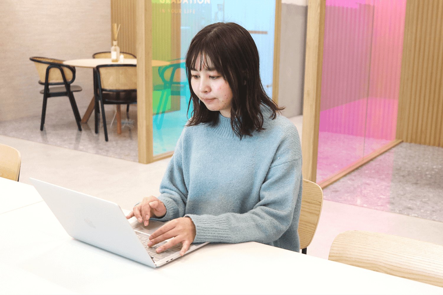 コワーキングスペースの窓際テーブルでノートPCを操作するSAKIさん