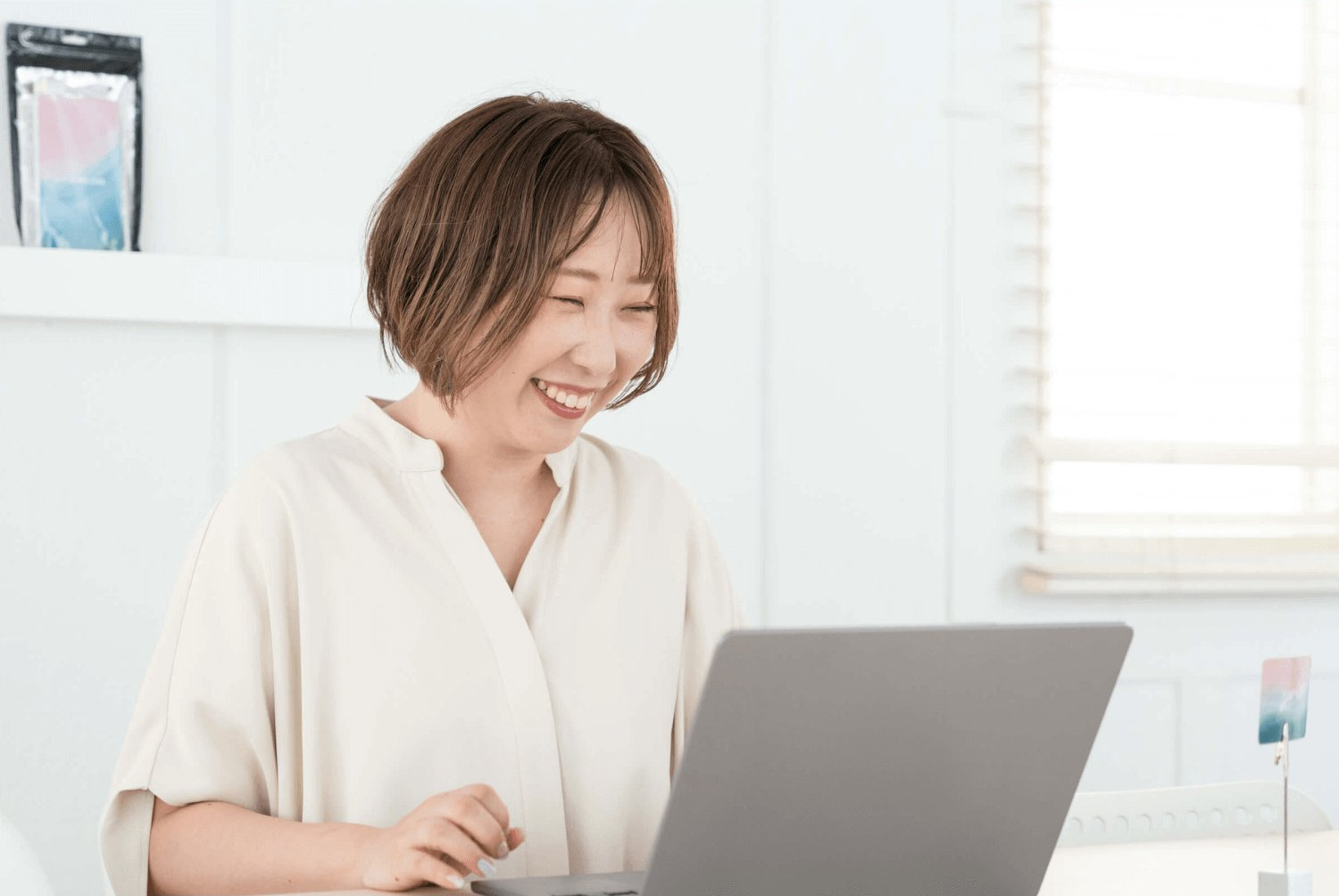 窓辺でノートパソコンに向かい微笑むリエさん