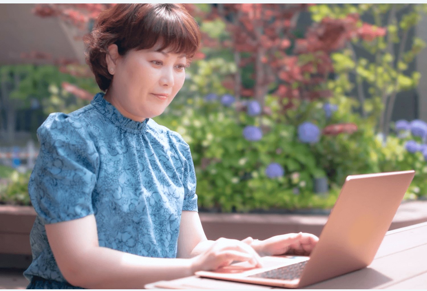 紅葉と紫陽花が咲く庭を背景に、屋外のテーブルでノートPCを操作する薫さん