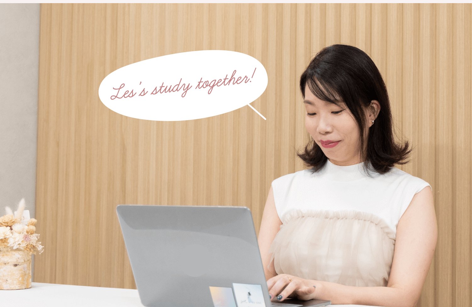木目の壁の前でノートパソコンに向かう直子さん。「Let's study together!」の手書き風吹き出し装飾