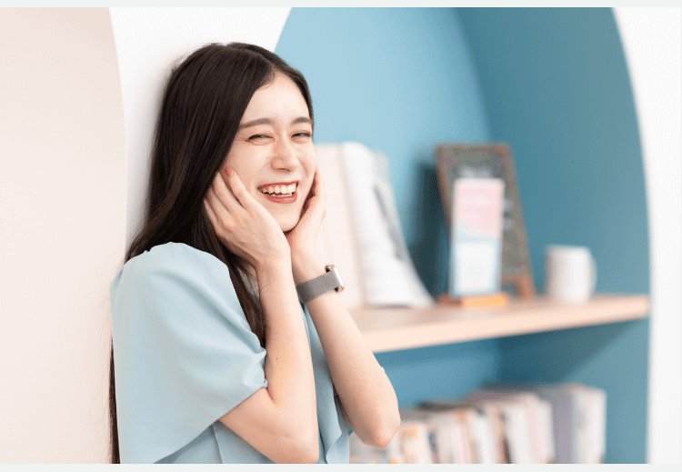 書棚を背景に、両手を頬に添えて笑うHinakoさん