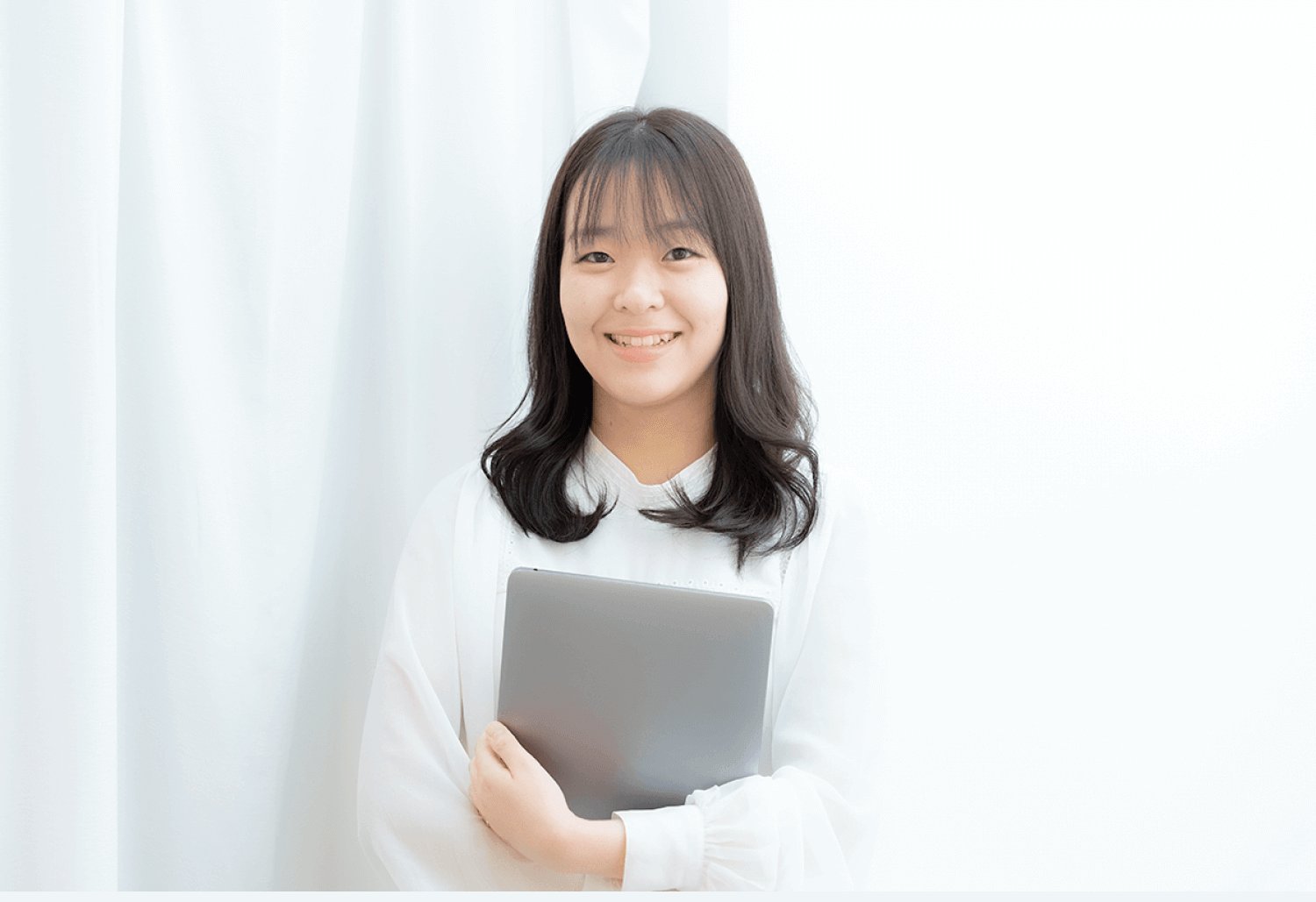 白いカーテンを背景に、タブレットを抱えて微笑むなこてんさん