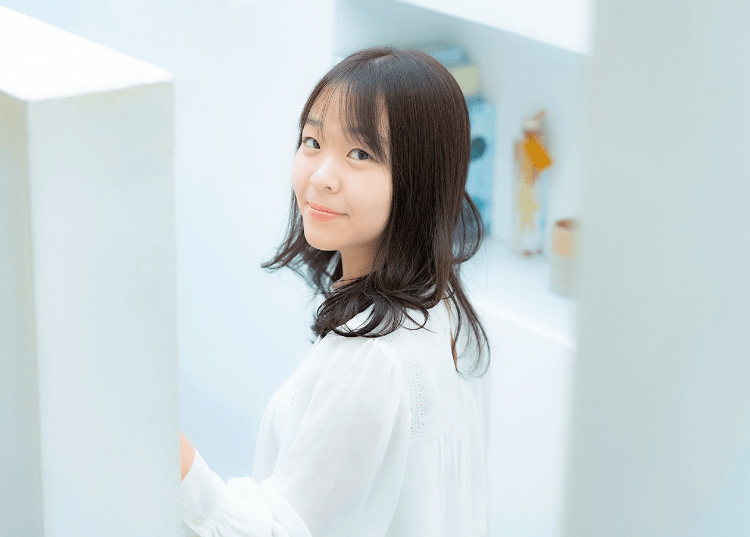 白い壁を背景に、こちらを見て微笑むなこてんさんのポートレート