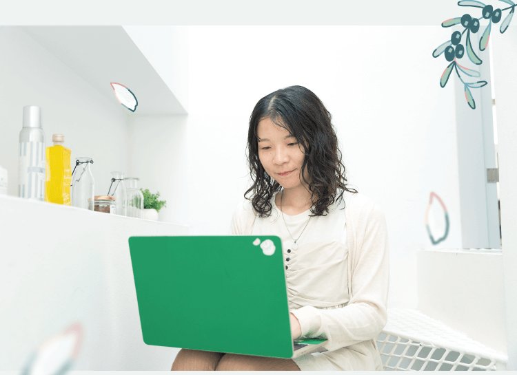 キッチンカウンターで緑のノートPCを操作する本人。自然光の入る室内