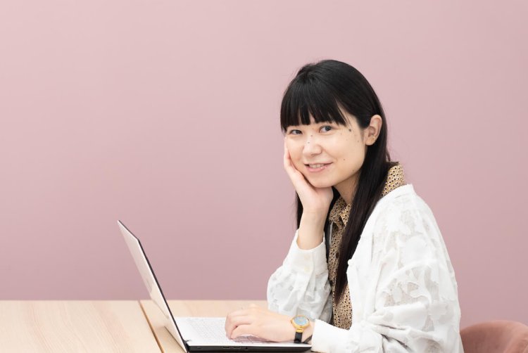 ピンク系の壁の前でノートPCに向かい、頬杖をついて微笑むちゃみさん