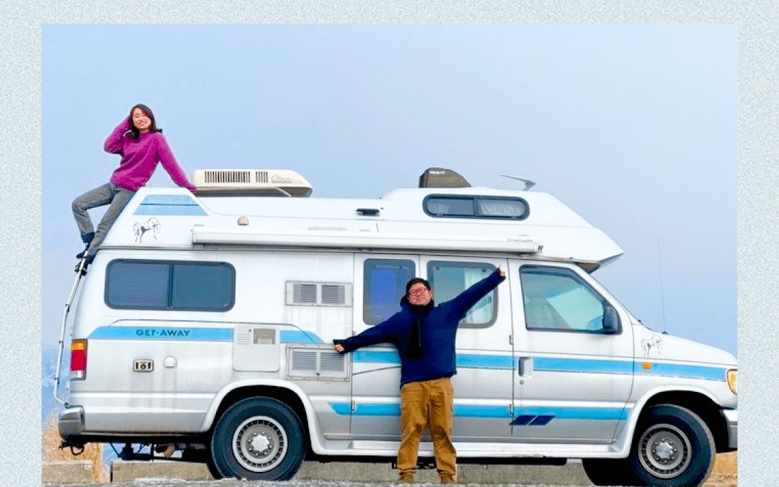 キャンピングカーの前でパートナーと二人、車の屋根に乗って手を挙げる可部ちゃんと両手を広げるパートナー