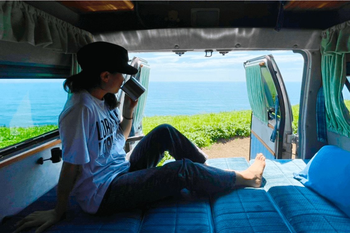 キャンピングカーの車内で、コーヒーを片手に海を眺める可部ちゃん