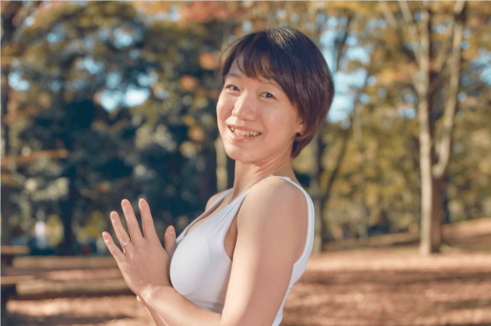 ヨガのポーズをとりながら微笑む、屋外の紅葉の中のちっひーさん