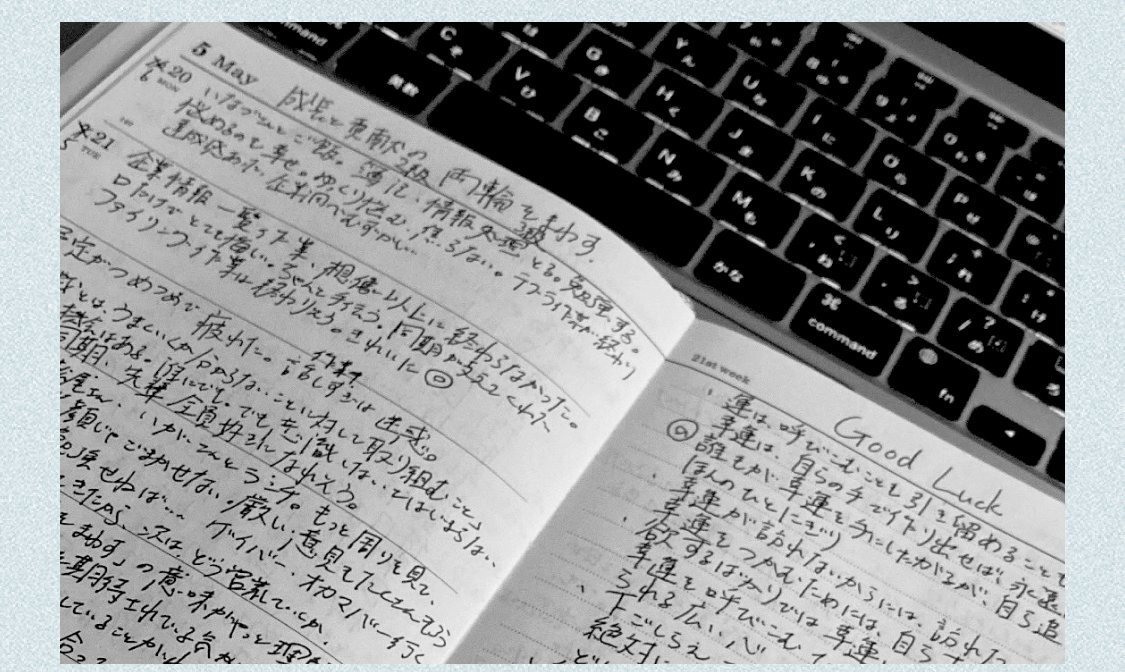 手帳に書き込まれた手書きのメモとノートPCのキーボード(モノクロ調)