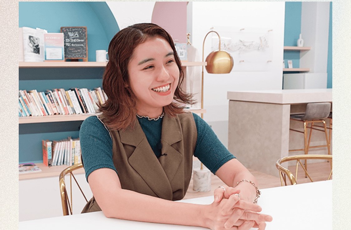 SHElikesのラウンジで笑顔で語る杏珠さん(本棚とスタンドライトのある部屋)