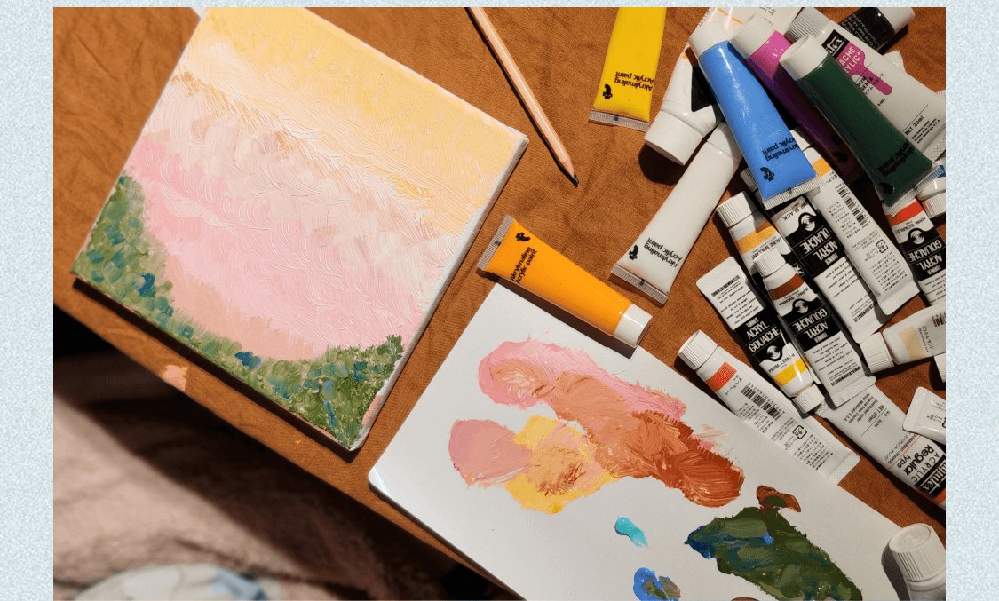 制作中のキャンバスと絵の具チューブ・パレットが並ぶ作業机