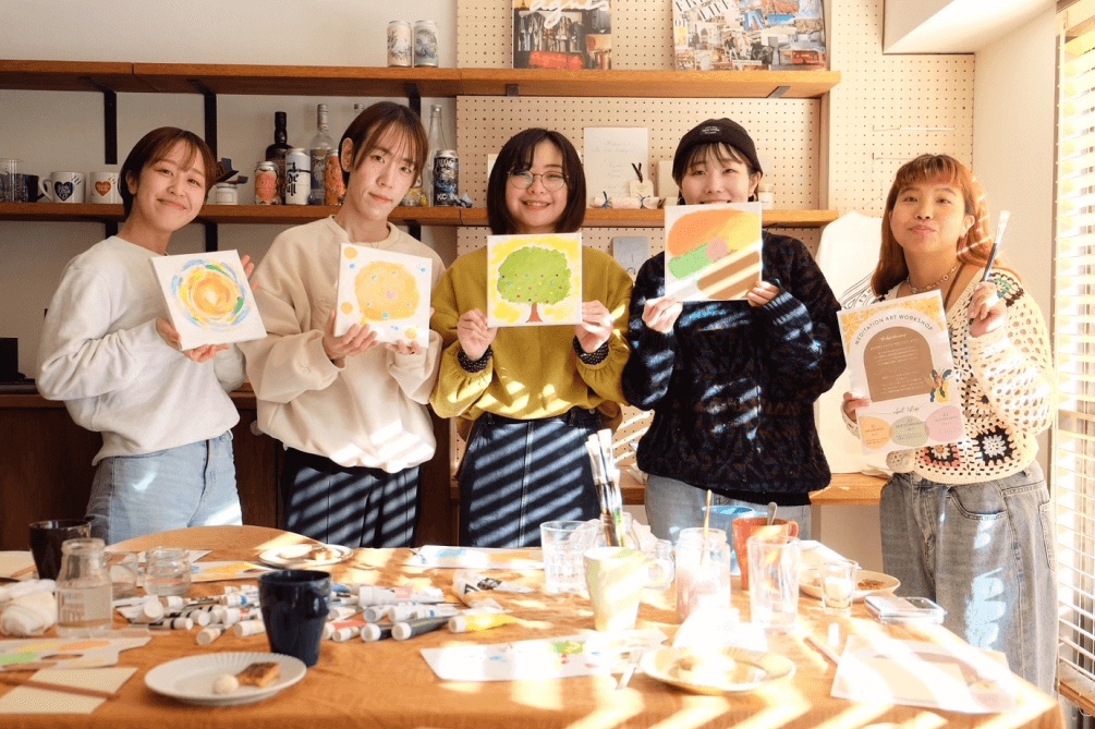 5人の女性がそれぞれの絵を掲げて笑顔で並ぶワークショップの記念撮影