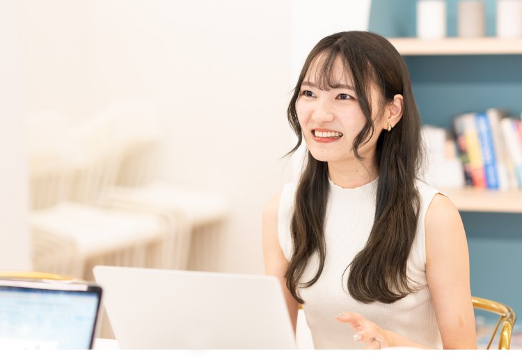 本棚を背景にノートPCを操作しながら微笑むさきさん