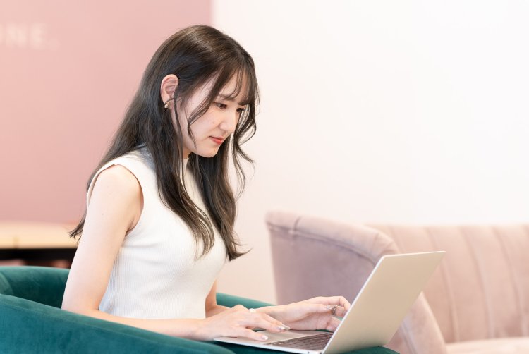 ピンク系の壁を背景にノートPCを操作するさきさん