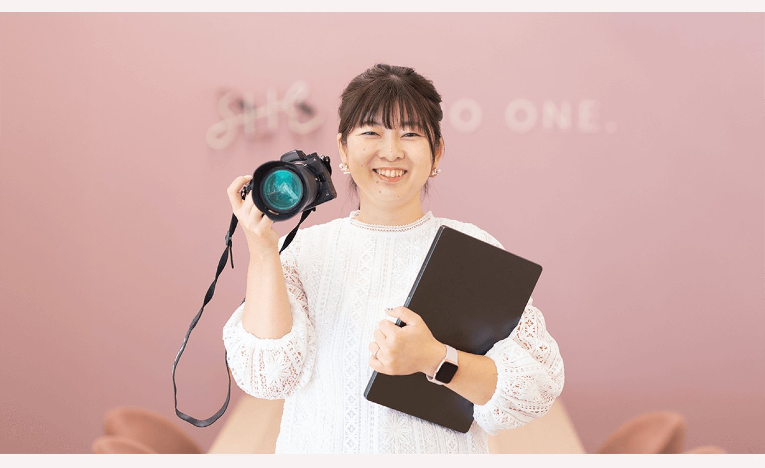 SHElikesのラウンジでカメラとノートPCを抱えて微笑むくみさん