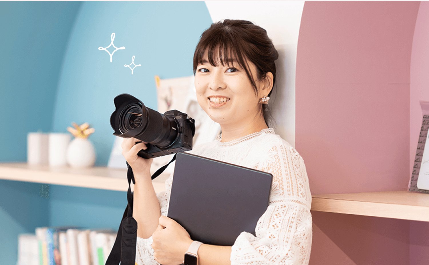 SHElikesのラウンジでカメラとノートPCを抱えて微笑むくみさん