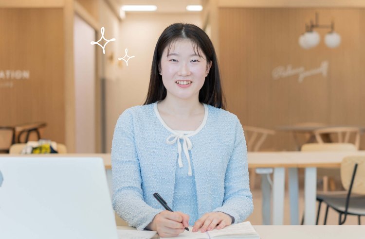 木目調のカフェスペースでノートPCに向かい微笑むもんかさん
