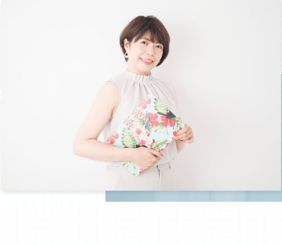 白い壁にもたれ花柄クラッチを持つ利穂さん