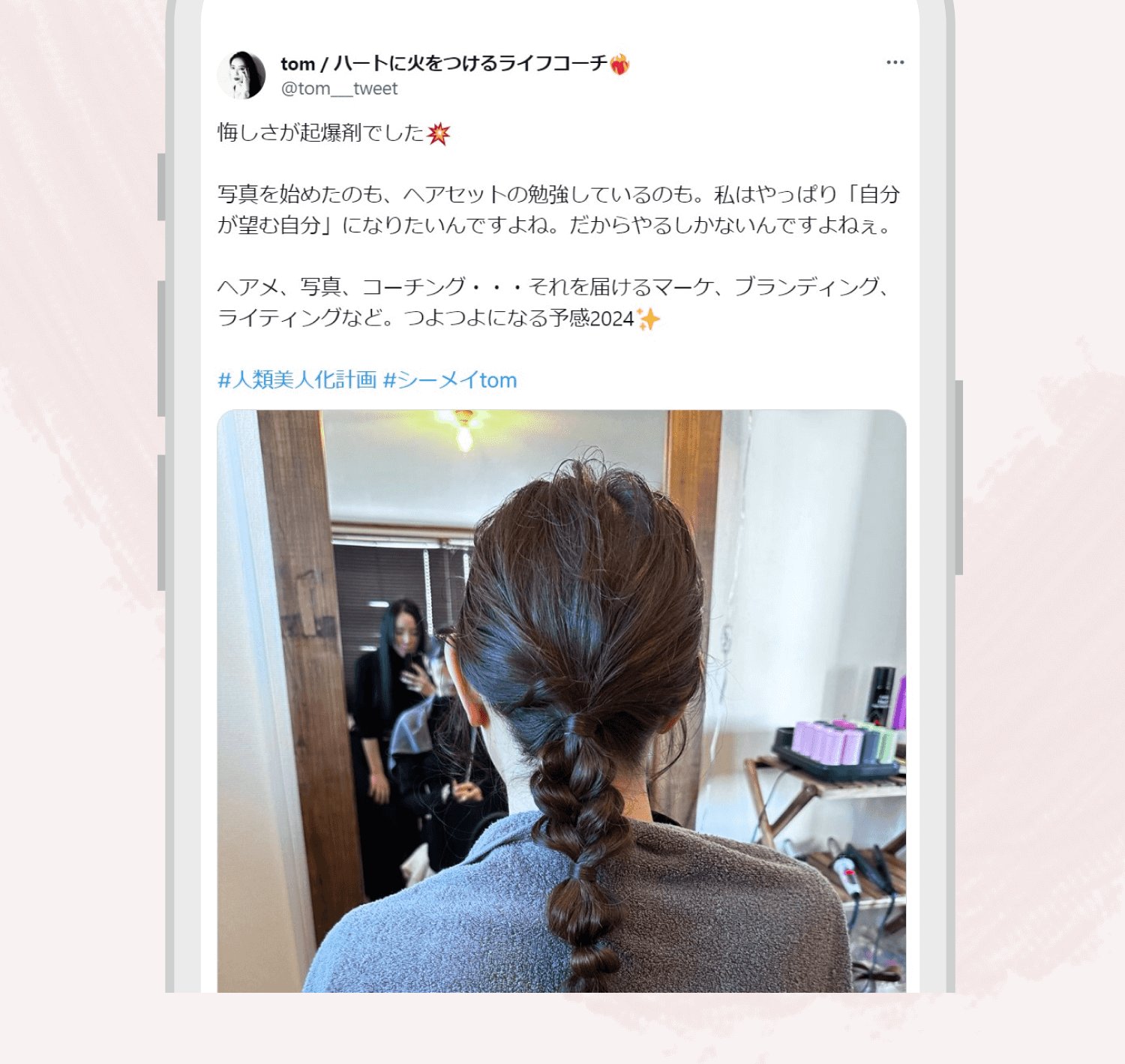 スマートフォンのtomさん本人のX（旧Twitter）投稿画面のスクリーンショット。投稿文「悔しさが起爆剤でした。写真を始めたのも、ヘアセットの勉強しているのも。私はやっぱり「自分が望む自分」になりたいんですよね。だからやるしかないんですよねぇ。ヘアメ、写真、コーチング・・・それを届けるマーケ、ブランディング、ライティングなど。つよつよになる予感2024」の下に、鏡越しにヘアセットの練習をする様子の写真が添付されている