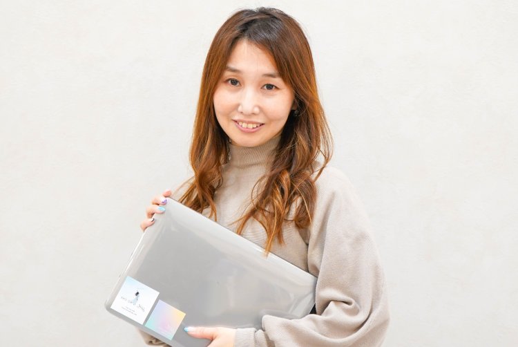 ノートPCケースを抱えて微笑むのんさんのポートレート