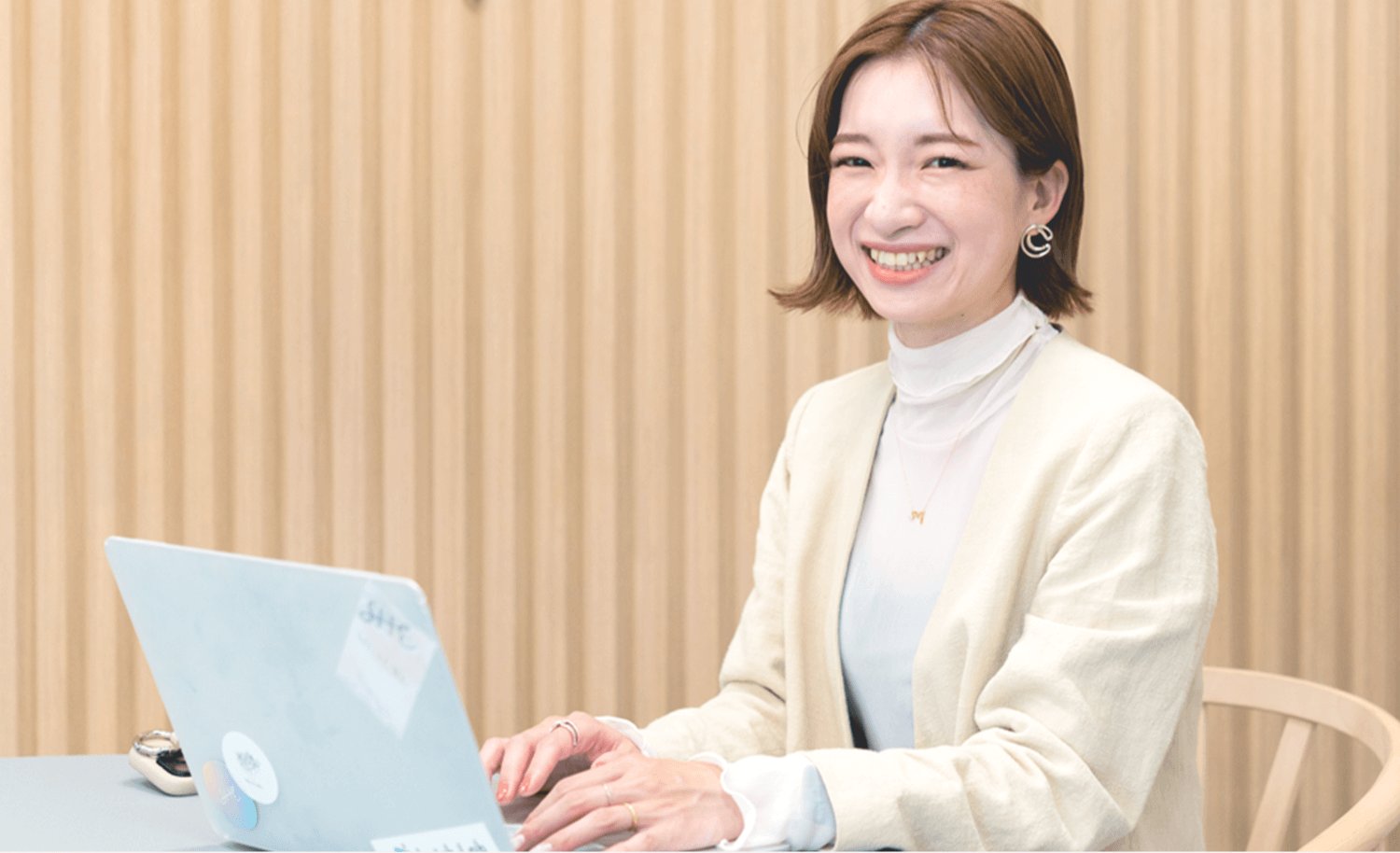 木目の壁を背に、ノートパソコンに向かい微笑むJURIさん