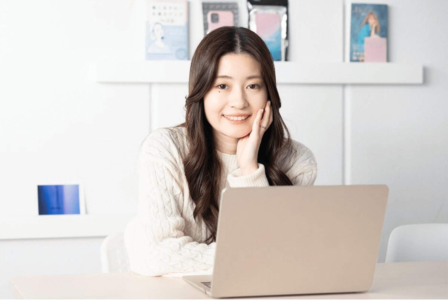 棚に囲まれたデスクでノートPCに向かい、頬杖をついて微笑むあやのえるさんの写真