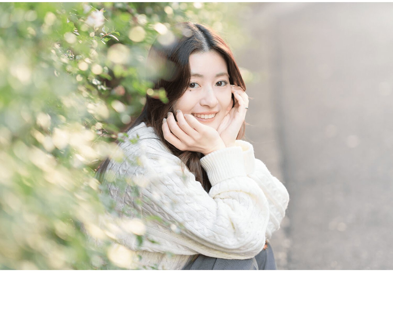 緑と白い花のそばで頬に手を添えて微笑むあやのえるさんの写真