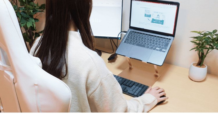 デュアルモニターとノートPCが並ぶデスクで作業する京香さんの後ろ姿