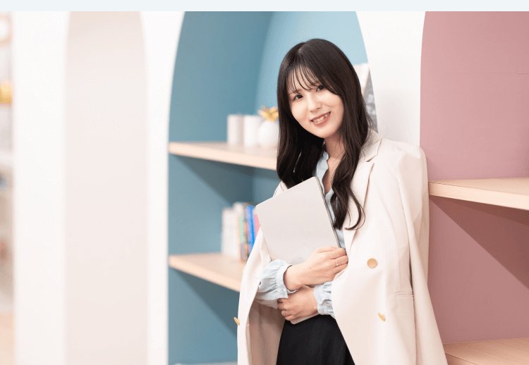 本棚のアーチを背景に、フォルダを抱えて微笑むKaorukoさん