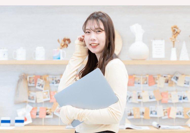明るい店舗のような空間でノートPCを抱えながら振り返って微笑むしゅうまいさん