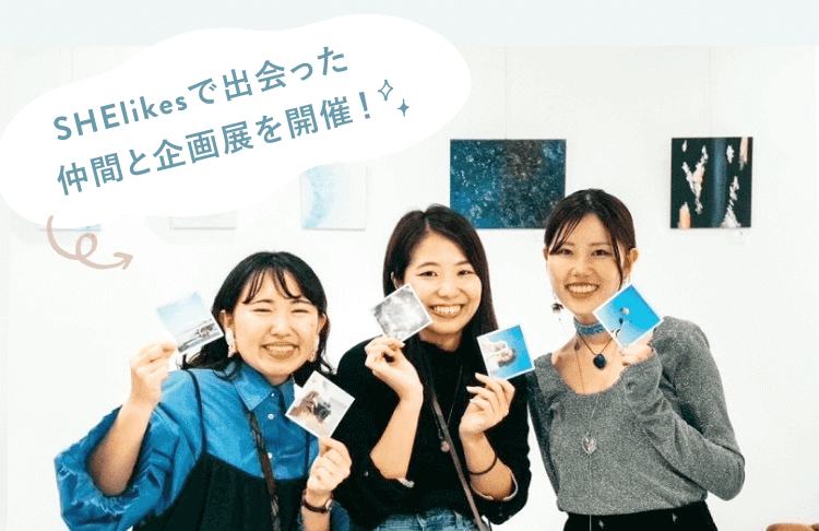 SHElikesで出会った仲間3人と企画展を開催したときの写真。SHEロゴ入りのポラロイド写真を手に笑顔で並ぶ様子