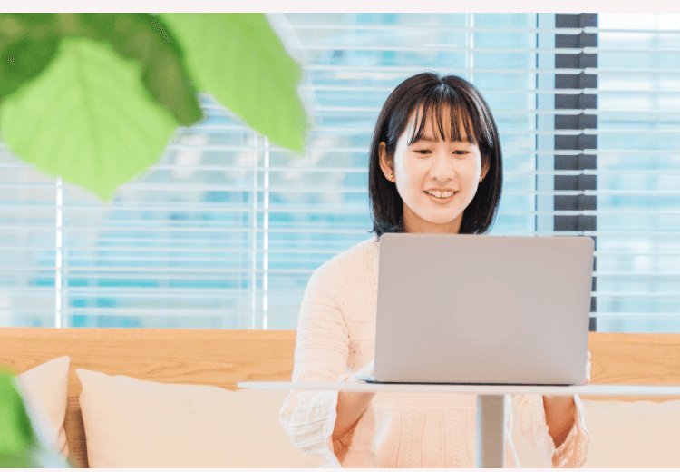 観葉植物のある明るい部屋のカウンター席でノートPCに向かい微笑むりこぴんさん