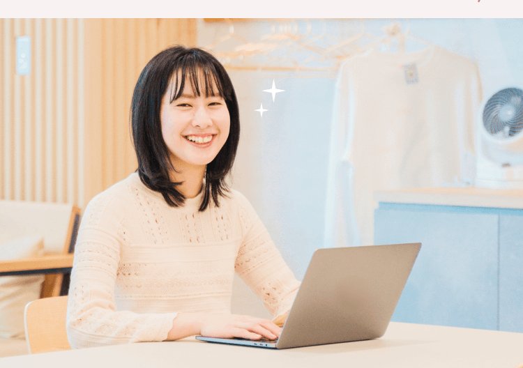 観葉植物・洋服ラックのある明るい部屋でノートPCに向かい微笑むりこぴんさん