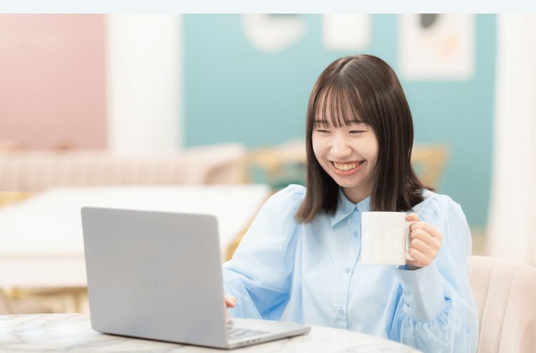 テラス風の室内でマグカップを手にノートPCに向かい微笑むHicaさん