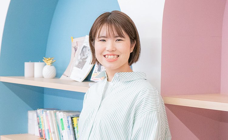 青とピンクのアーチ型の棚を背景に微笑むまほさんの写真
