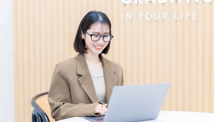 木目調の壁の前でノートPCを操作するまゆこさん