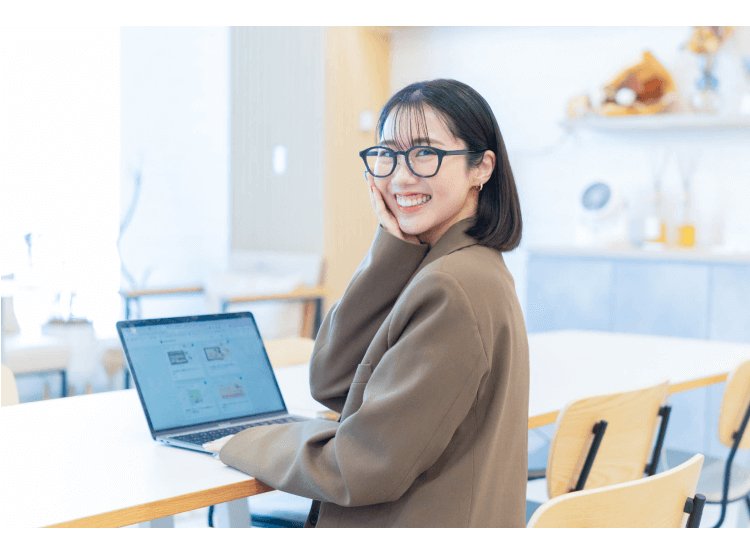ノートPCの前で振り返って微笑むまゆこさん
