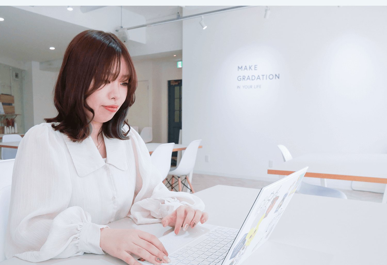 白い壁のオフィスでノートPCに向かい微笑む秋葉みやびさん