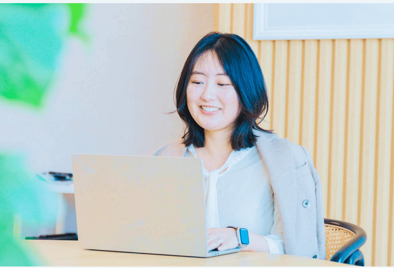 木製ルーバー壁を背景にノートPCに向かい微笑むしほきちさん