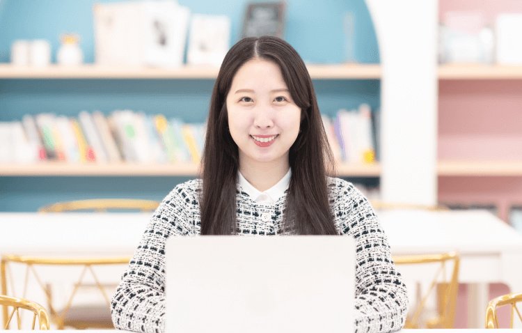 本棚のある室内でノートPCに向かうかんなさん