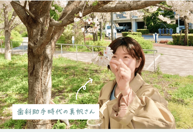 桜の木の下で微笑む真帆さんの写真。「歯科助手時代の真帆さん」の文字が添えられている