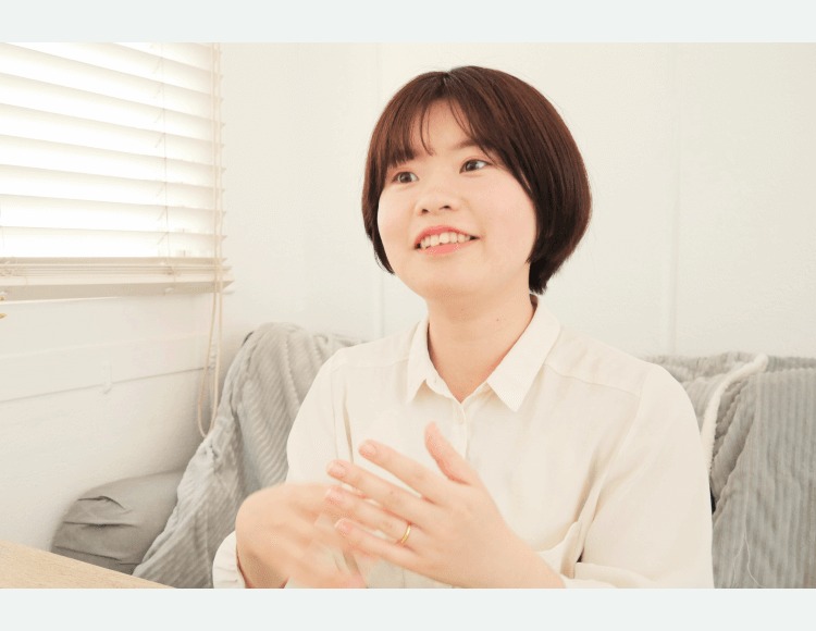 室内のソファで微笑みながら話す真帆さんの写真