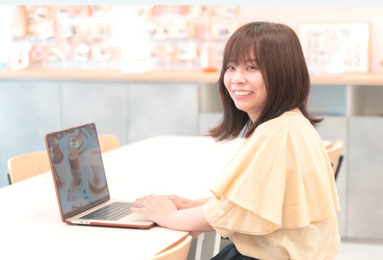 ノートPCに向かいながらこちらを振り返り微笑むIKUMIさんの写真