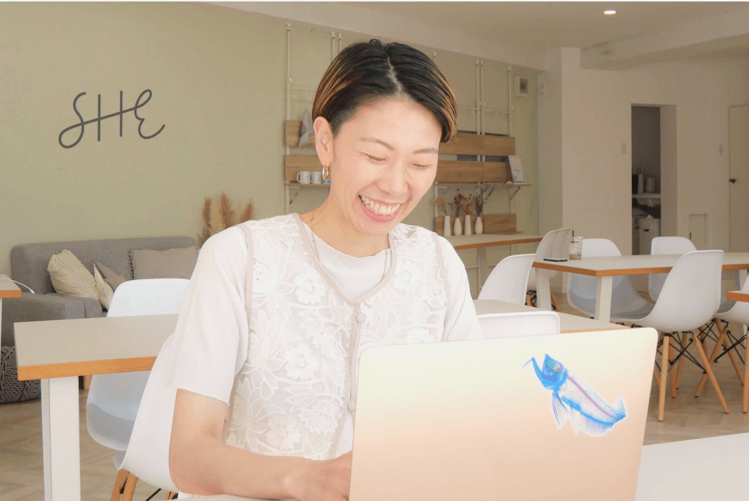 SHEのカフェスペースでノートPCに向かい微笑むtotoさん