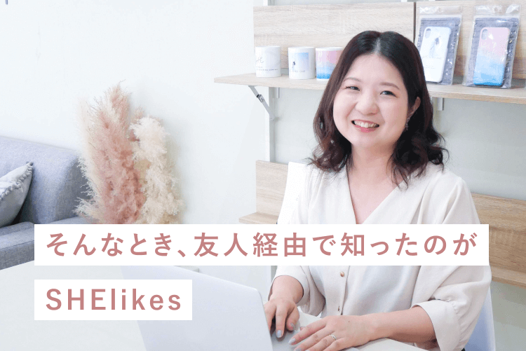 白い壁の部屋でノートPCを操作しながら微笑むきなこさんの写真。手前にドライフラワー、背後の棚にキャンドルやスマホケースが飾られている。「そんなとき、友人経由で知ったのがSHElikes」という白とサーモンピンクのラベル帯が写真下部に重なる