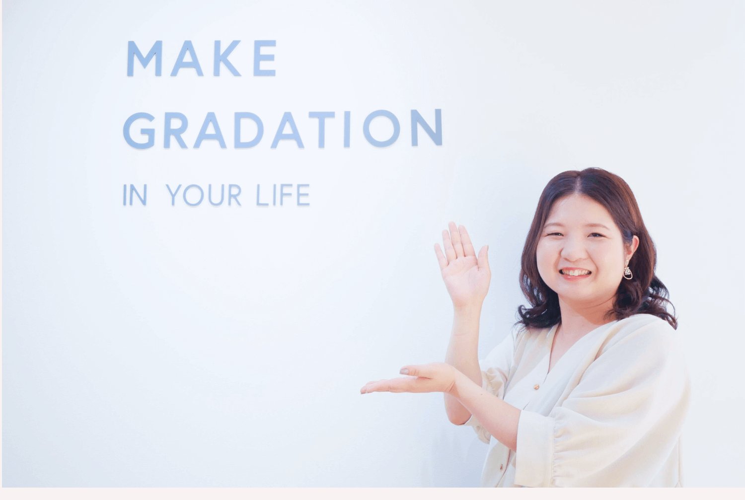 「MAKE GRADATION IN YOUR LIFE」の壁アートの前でポーズをとるきなこさん