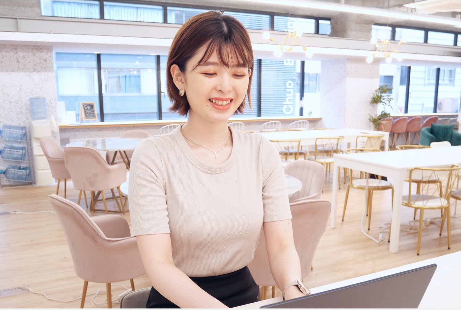 おしゃれなコワーキングスペースでノートPCを操作しながら微笑むシオリさん