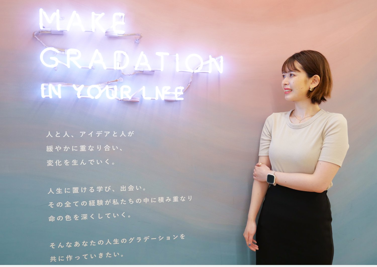 「MAKE GRADATION IN YOUR LIFE」のネオンサインの壁の前に立つシオリさん