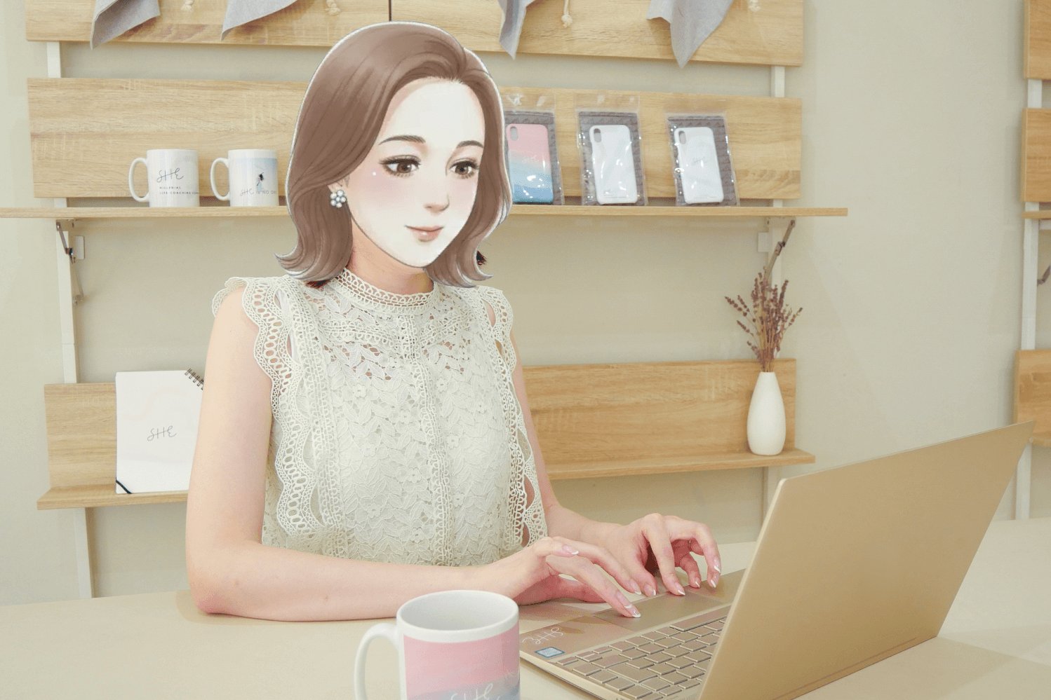 SHEのカフェスペースの壁に「SHE」のロゴ、棚にマグカップ・小物が並ぶ中、ノートPCに向かい微笑むmiiさん