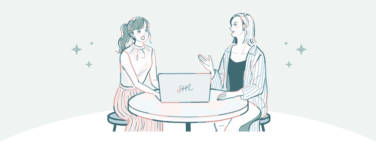 丸テーブルでノートPC（SHEロゴ入り）を囲んで話す2人の女性のイラスト